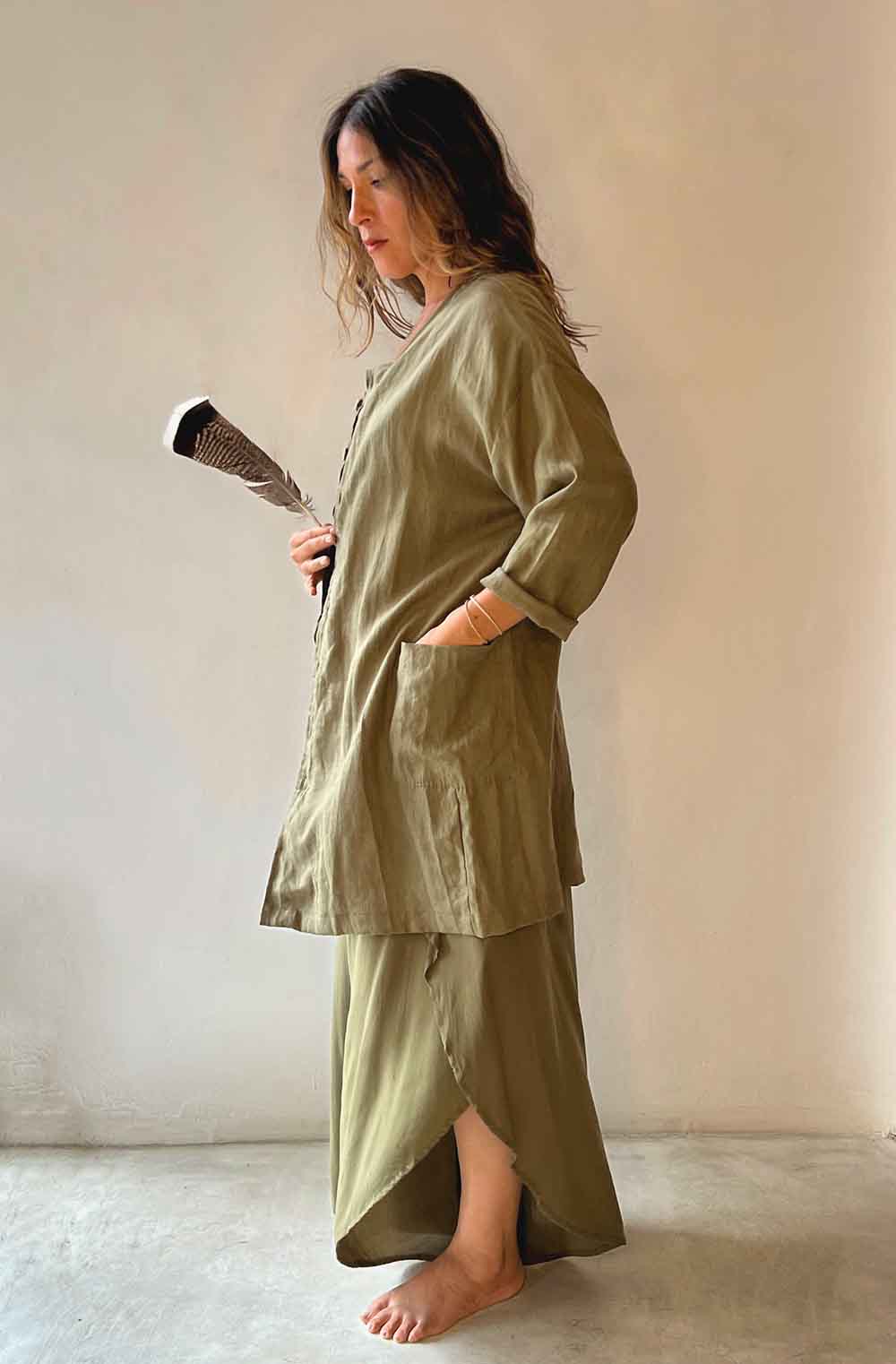 Woman wearing a green outfit holding a broom against a plain wall.