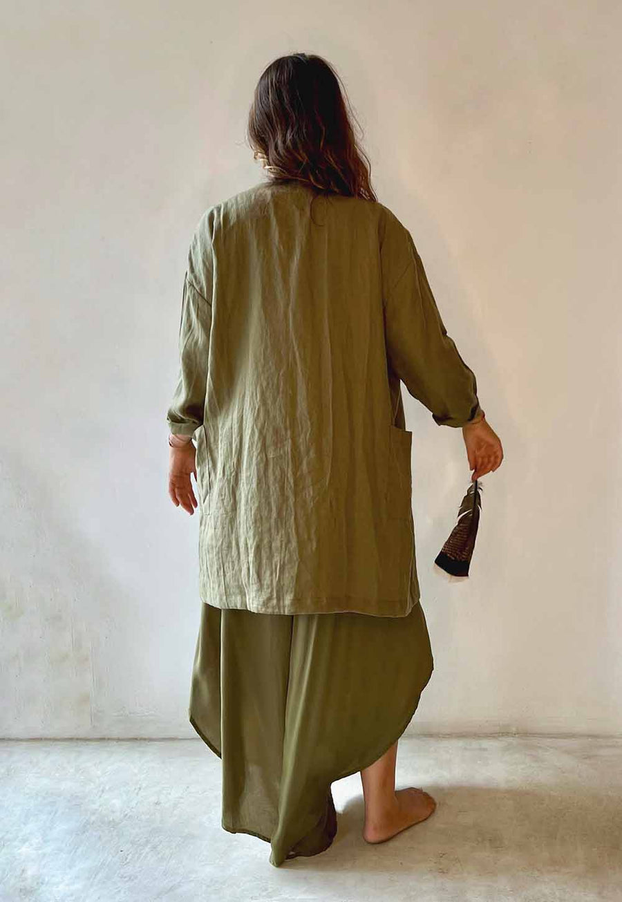 Person wearing an olive green outfit holding a small bag against a plain background