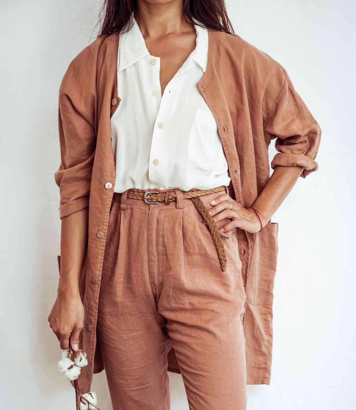 Person wearing a brown cardigan over a white shirt with a belt, on a plain background