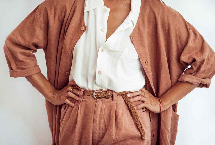 Person wearing a brown cardigan over a white shirt with a belt, on a plain background