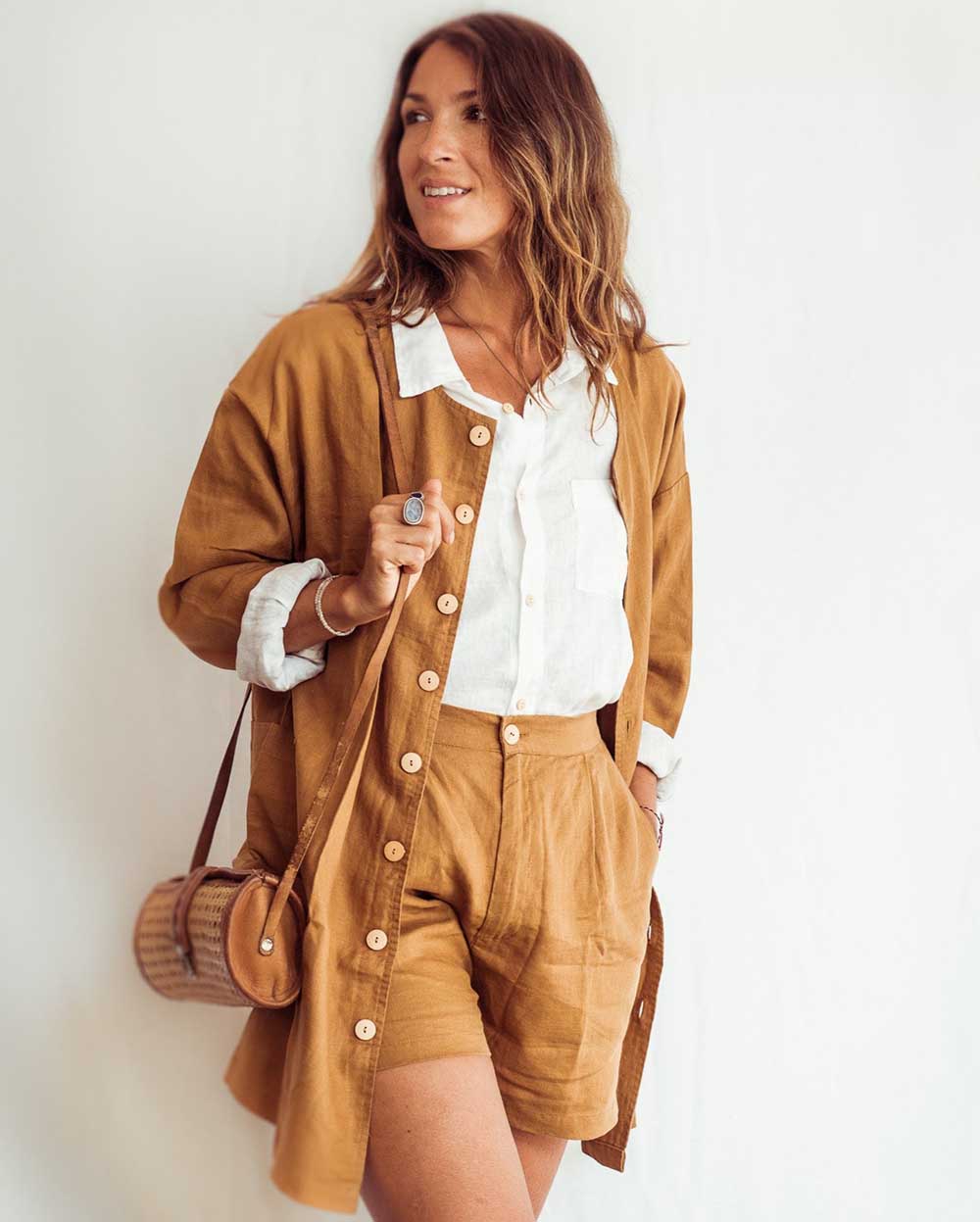 Woman wearing a mustard yellow outfit with a white shirt, holding a brown bag against a white background