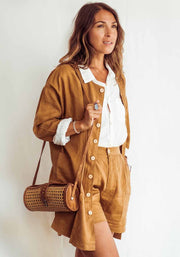 Woman wearing a brown outfit with a white shirt, holding a woven bag against a white background
