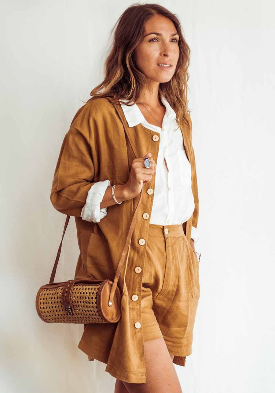 Woman wearing a brown outfit with a white shirt, holding a woven bag against a white background