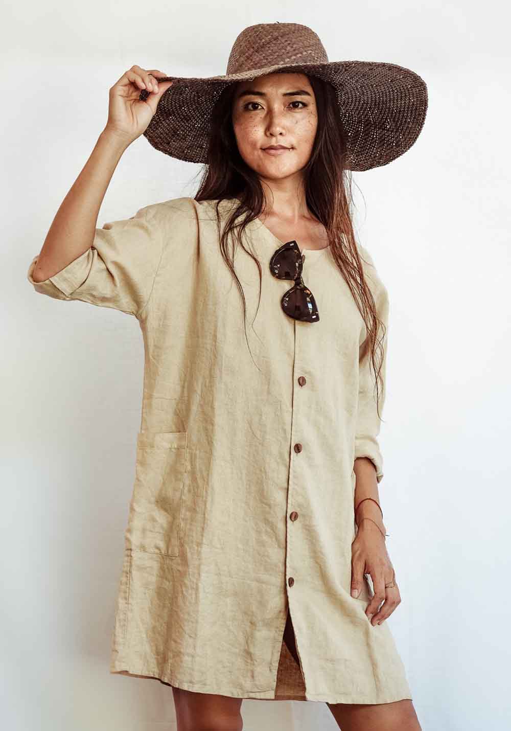Woman wearing a beige button-up dress and wide-brimmed hat on a white background