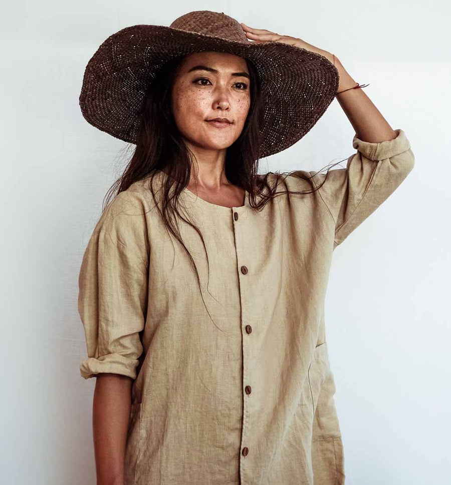 Woman wearing a wide-brimmed hat and beige shirt against a white background