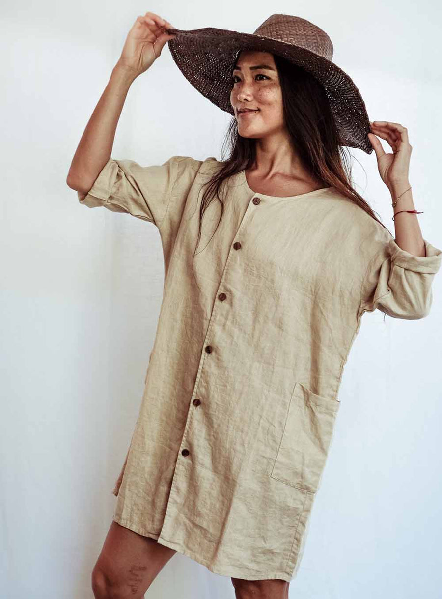 Woman wearing a beige dress and brown hat against a white background