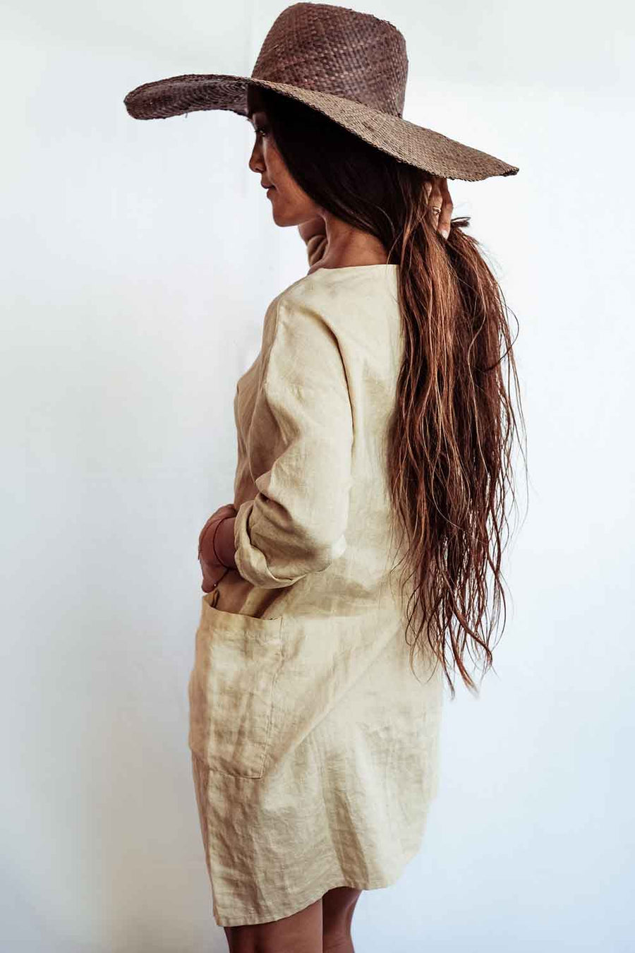Woman wearing a wide-brimmed hat and beige dress against a white background