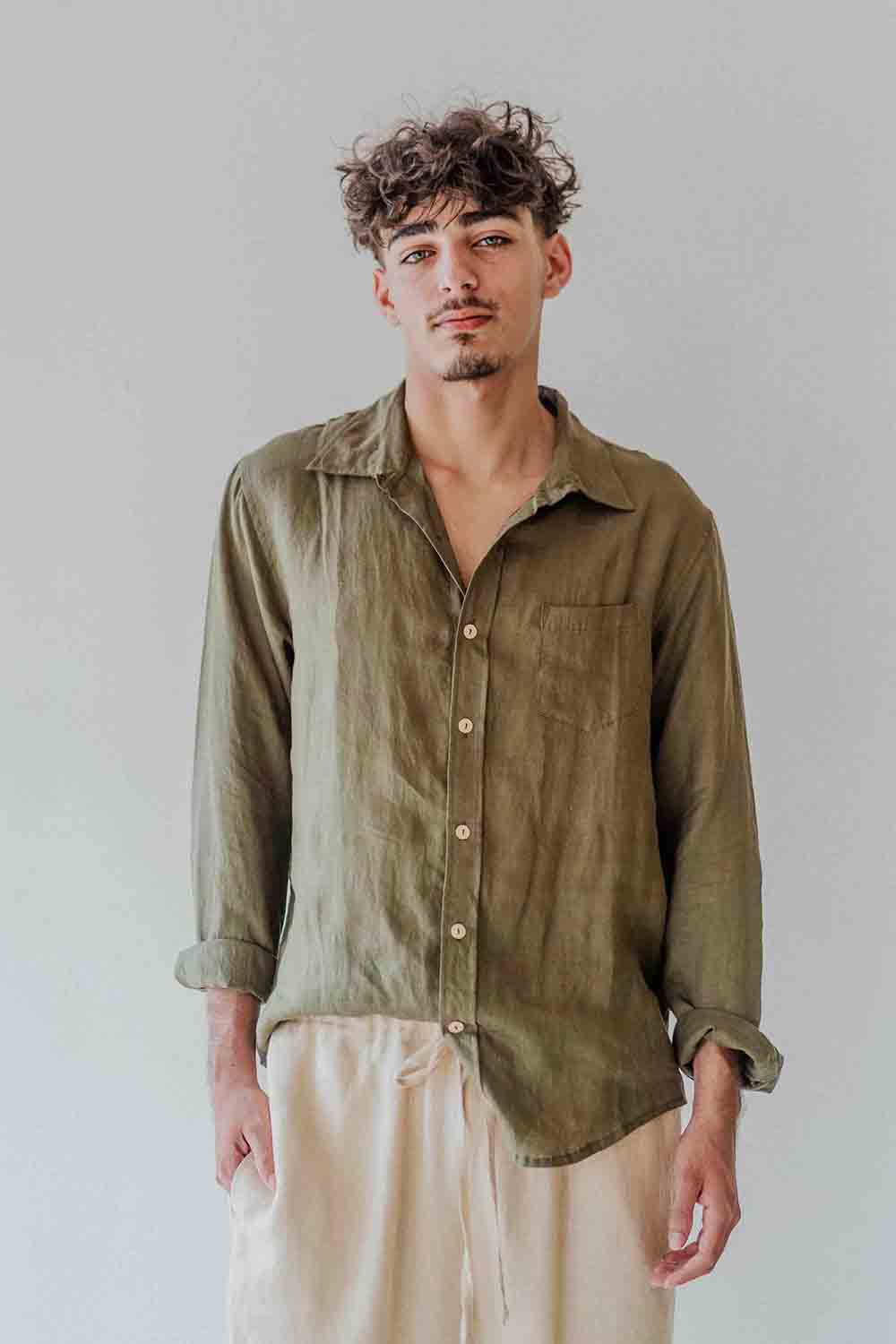 Man wearing an olive green shirt and beige pants against a plain background