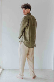 Person wearing an olive green shirt and beige pants against a white wall
