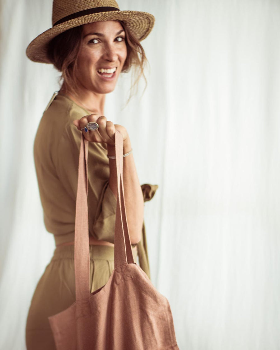 Woman wearing a straw hat and holding a pink tote bag against a white background