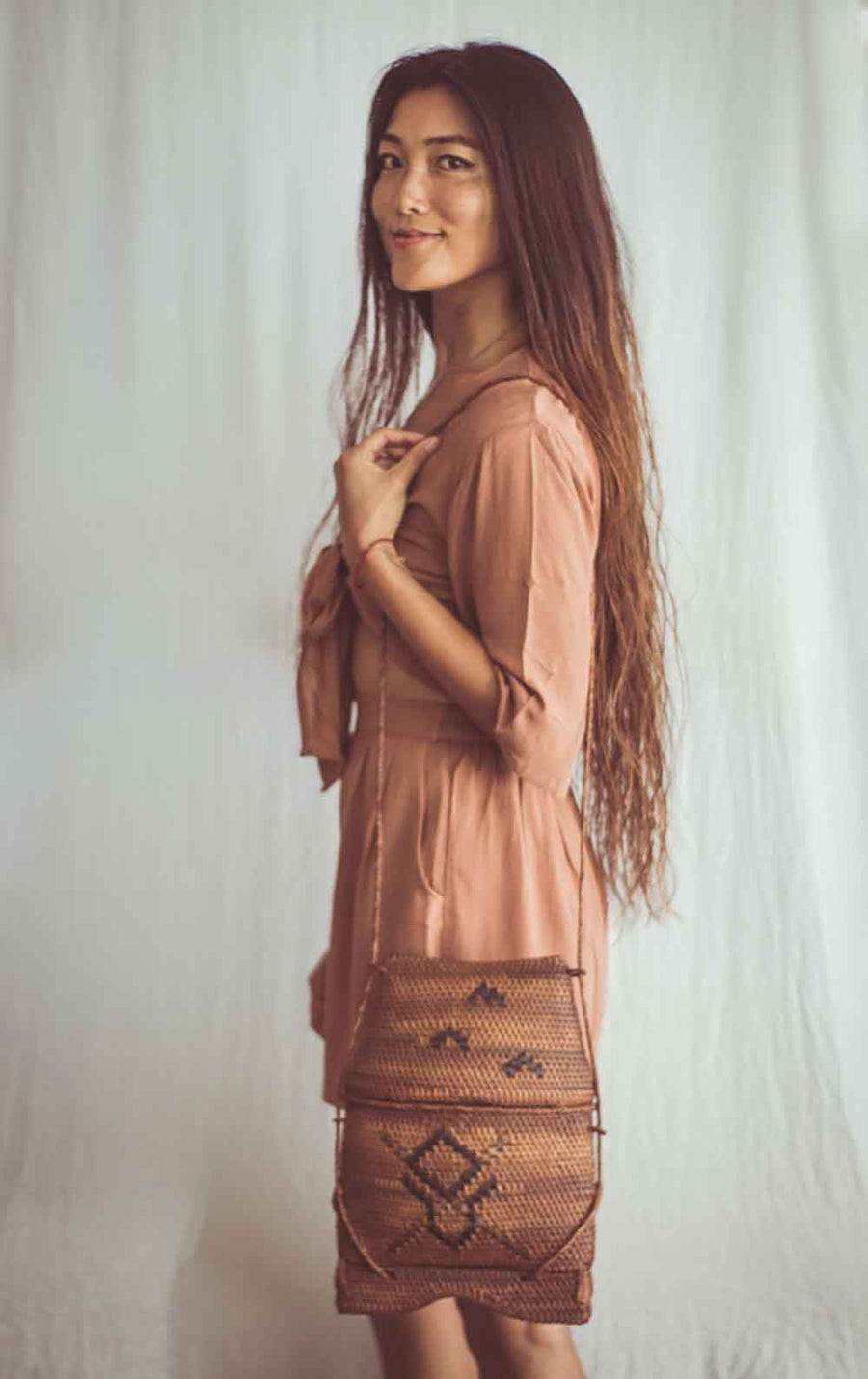 Woman holding a woven bag against a plain background