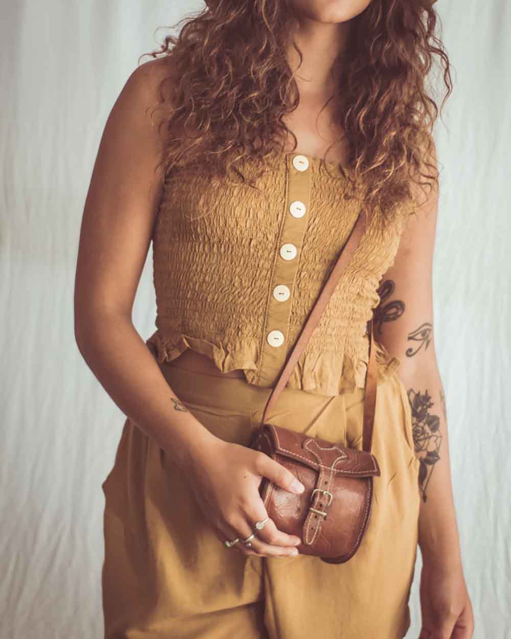Woman holding a brown leather bag wearing a mustard yellow sleeveless top and skirt.
