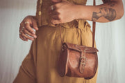 Person holding a brown leather handbag with a plain background