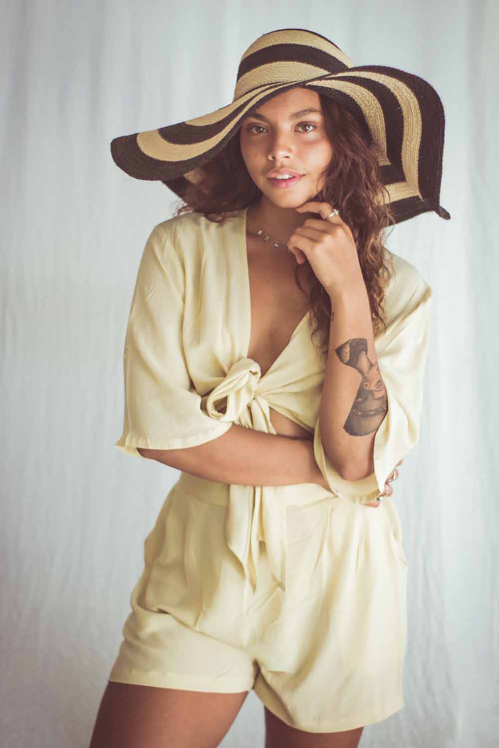 Woman wearing a light yellow outfit and large sun hat against a plain background