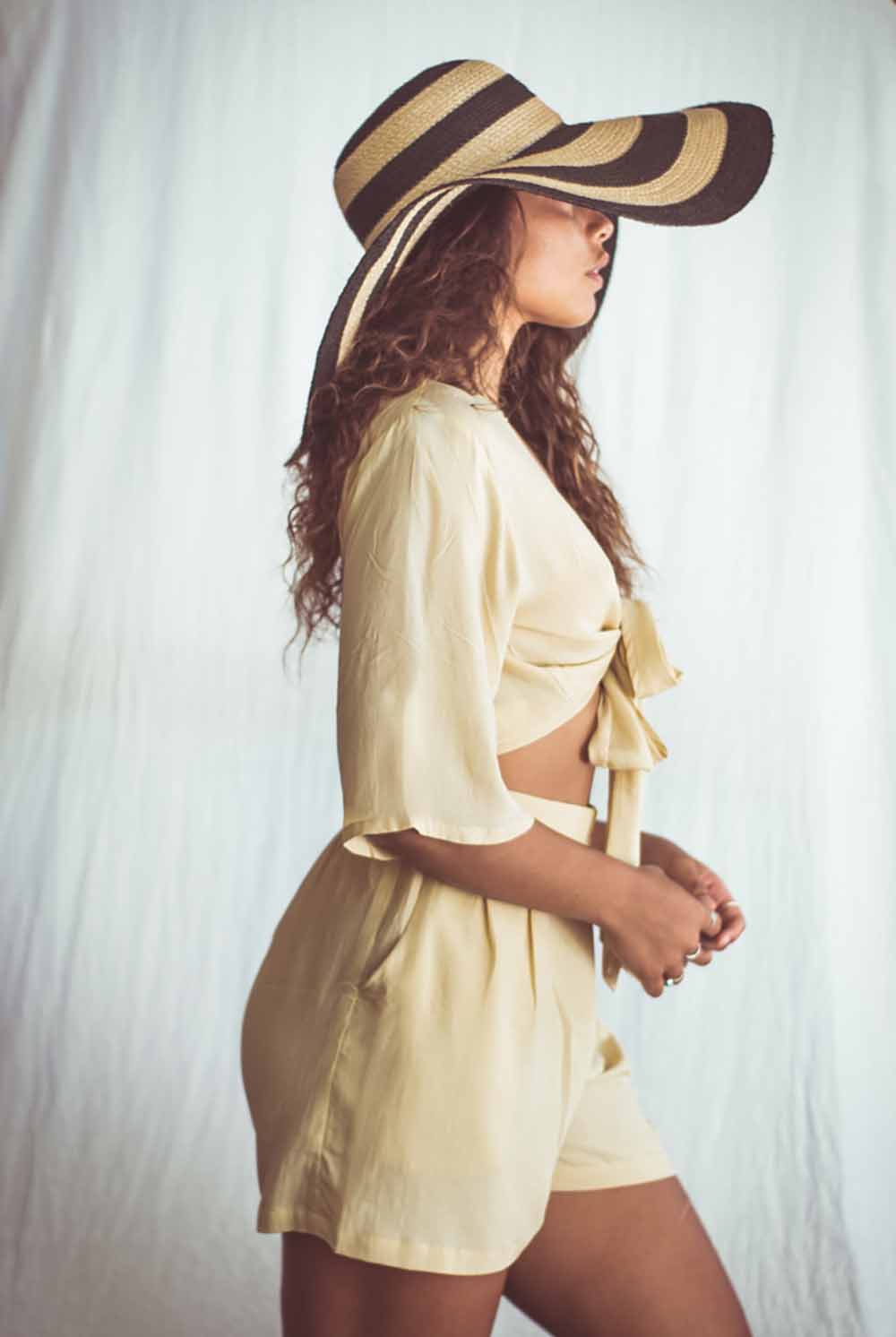 Woman wearing a yellow outfit and large sun hat against a white background