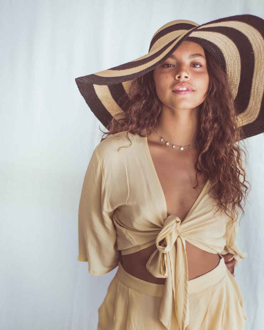 Woman wearing a beige outfit and large straw hat against a white background