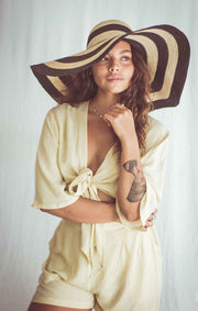 Woman wearing a beige outfit and large straw hat against a white background