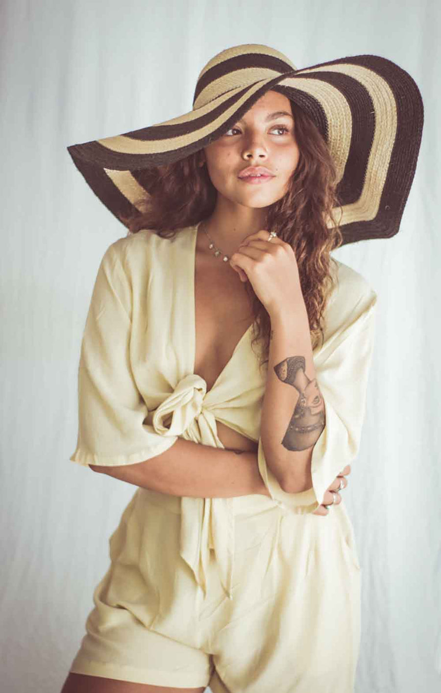 Woman wearing a beige outfit and large straw hat against a white background