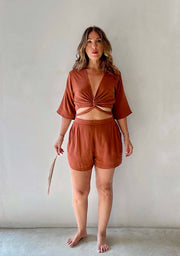 Woman wearing a brown outfit with a top and shorts against a plain background