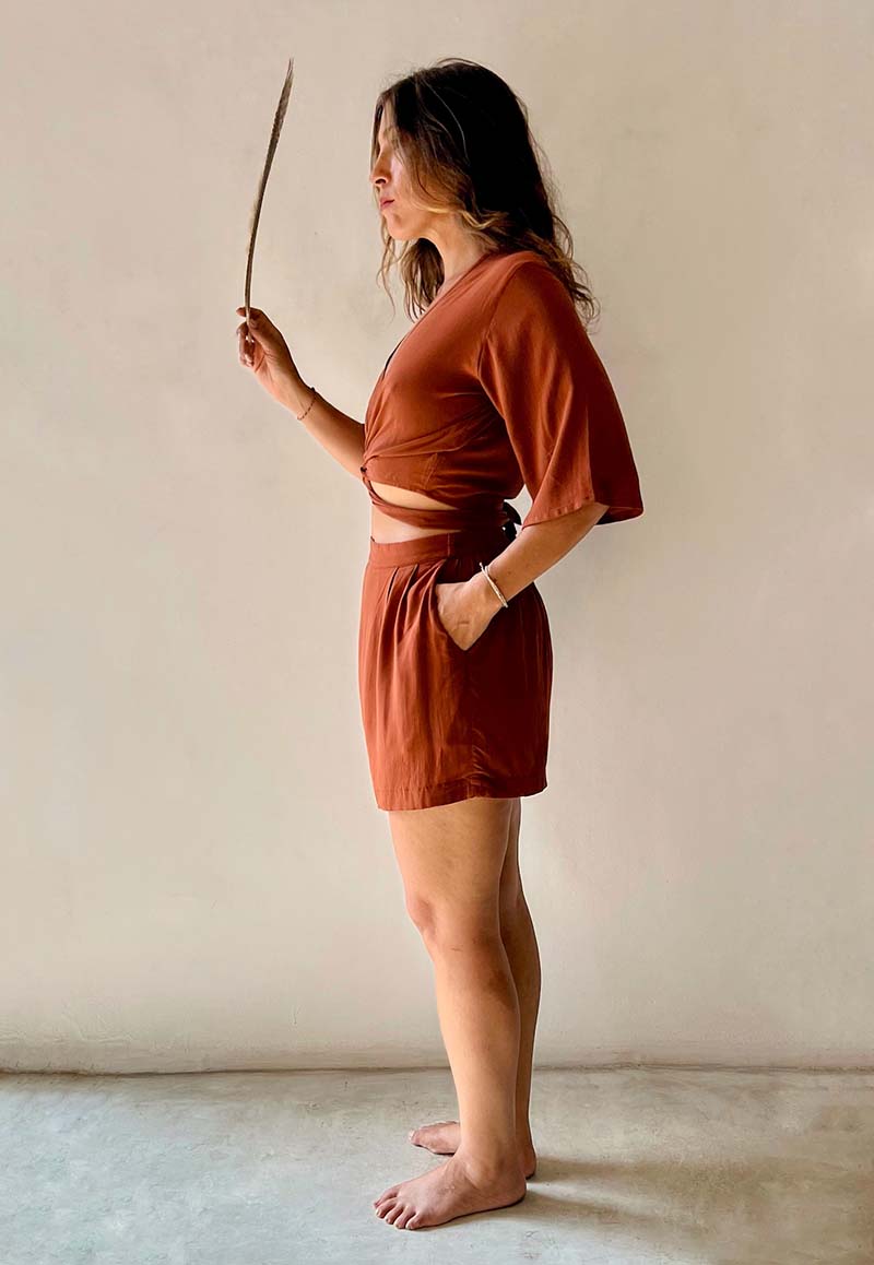 Woman wearing a rust-colored outfit holding a plant against a plain background