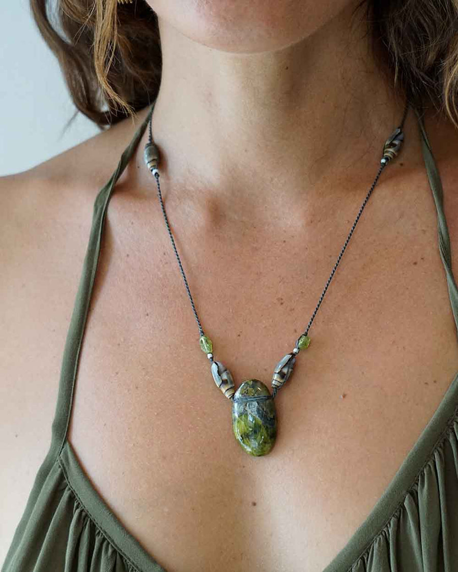 Necklace with a large green stone pendant worn by a person in an olive green top.
