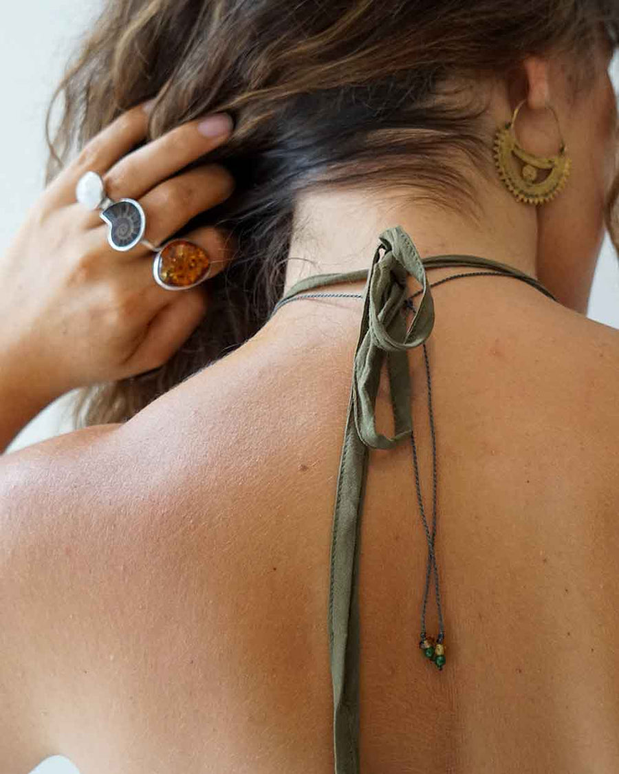 Close-up of a person wearing a green knotted choker with beads, gold hoop earrings, and rings.