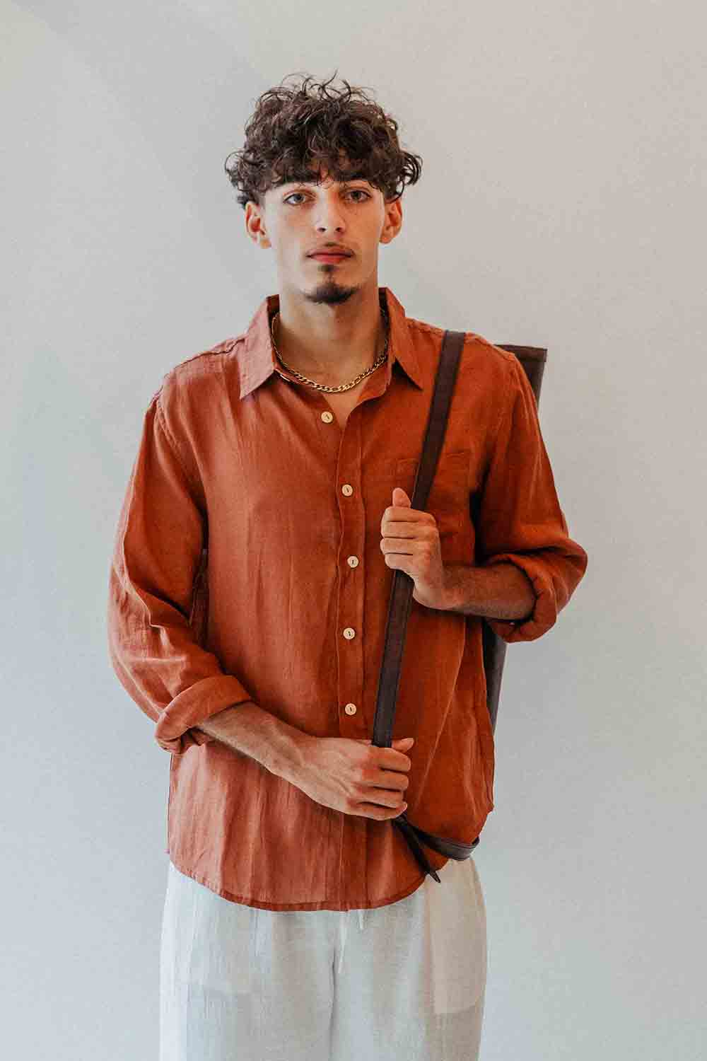 Man wearing a rust-colored shirt and light pants against a plain background