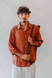 Man wearing a rust-colored shirt and light pants against a plain background