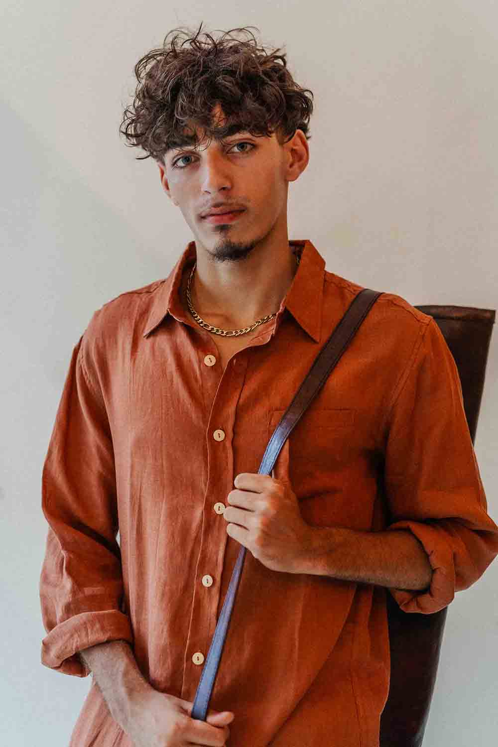 Man wearing an orange shirt holding a blue object against a neutral background