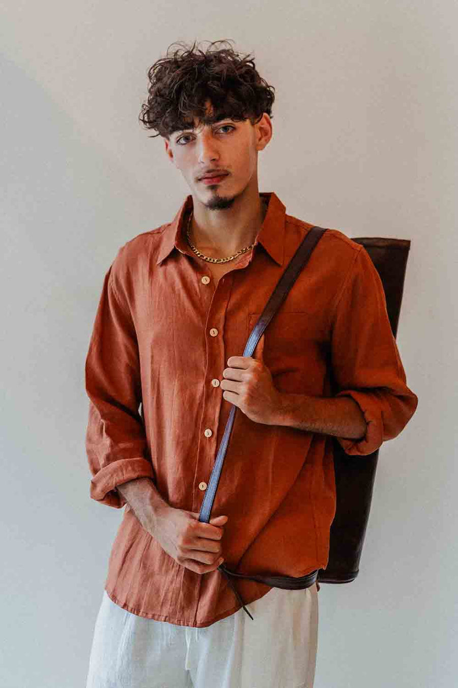 Man wearing a rust-colored shirt holding a brown bag against a plain background