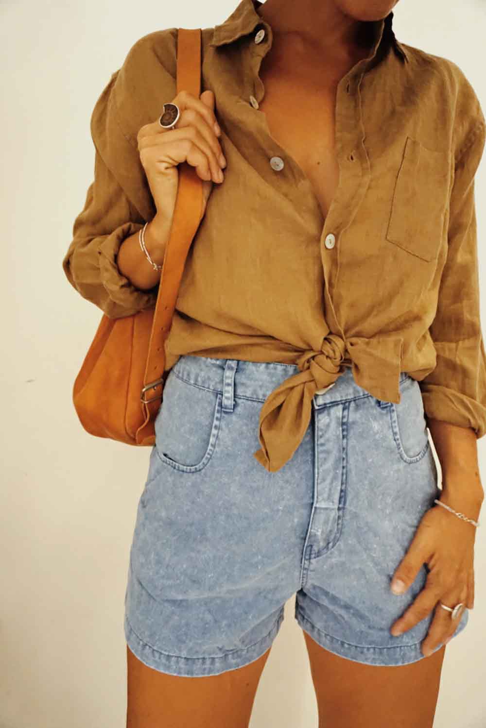 Person wearing a mustard yellow shirt and denim shorts, holding an orange bag.