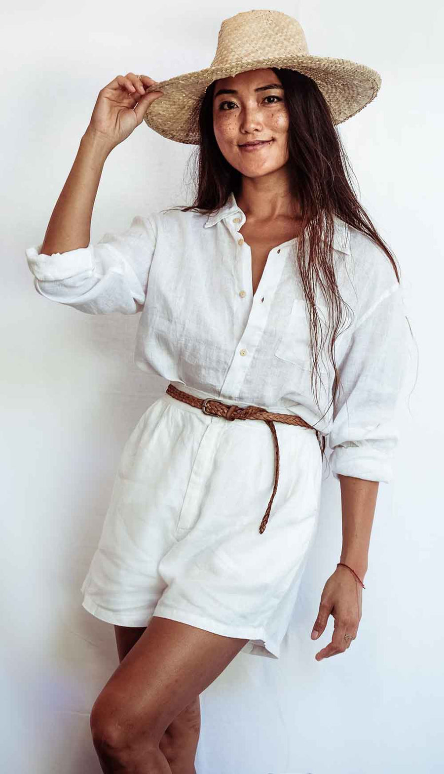 Woman wearing a white shirt and shorts with a wide-brimmed hat on a plain background