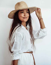 Person wearing a brown jacket, blue shorts, and a straw hat with an orange backpack on a plain background