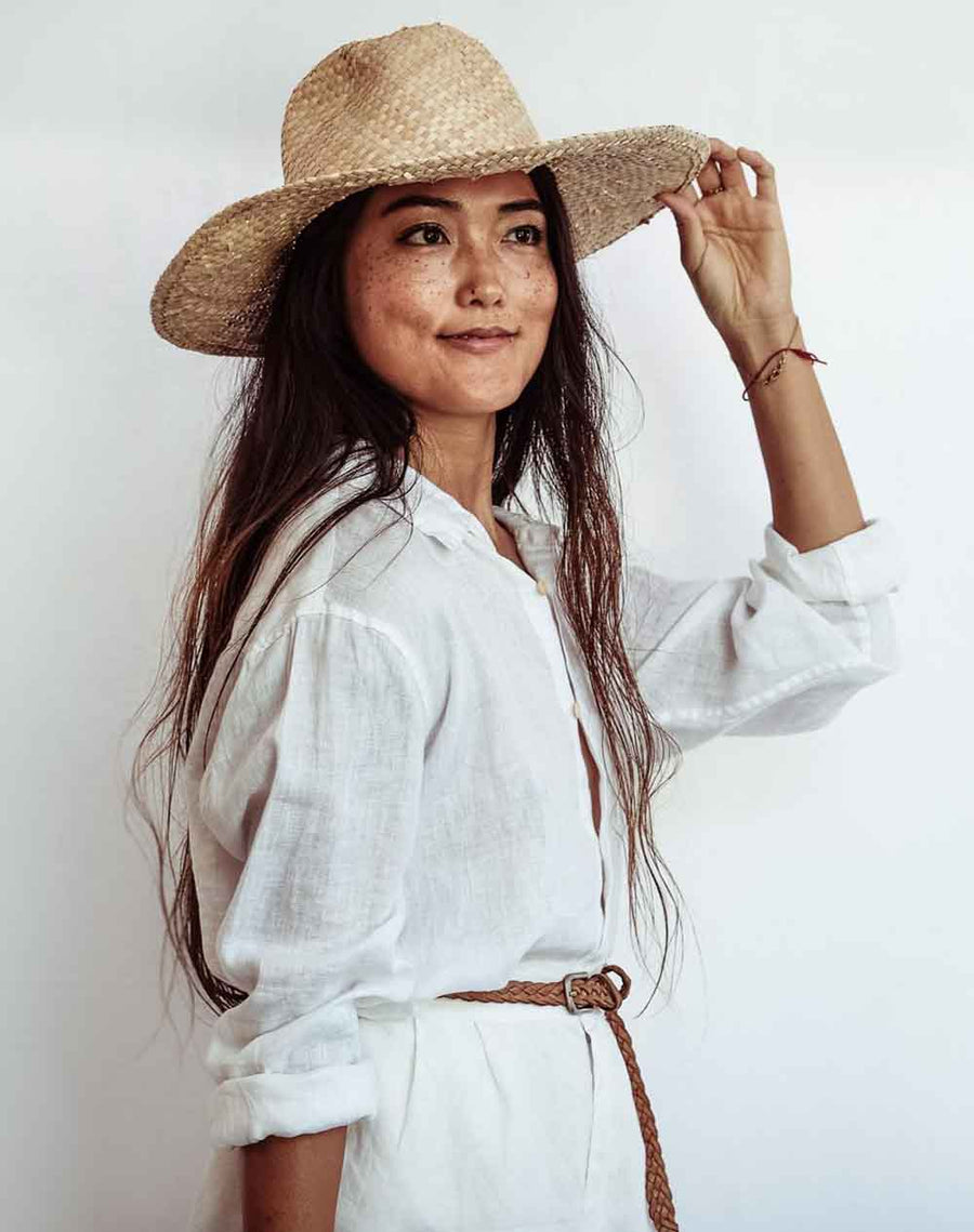 Person wearing a brown jacket, blue shorts, and a straw hat with an orange backpack on a plain background