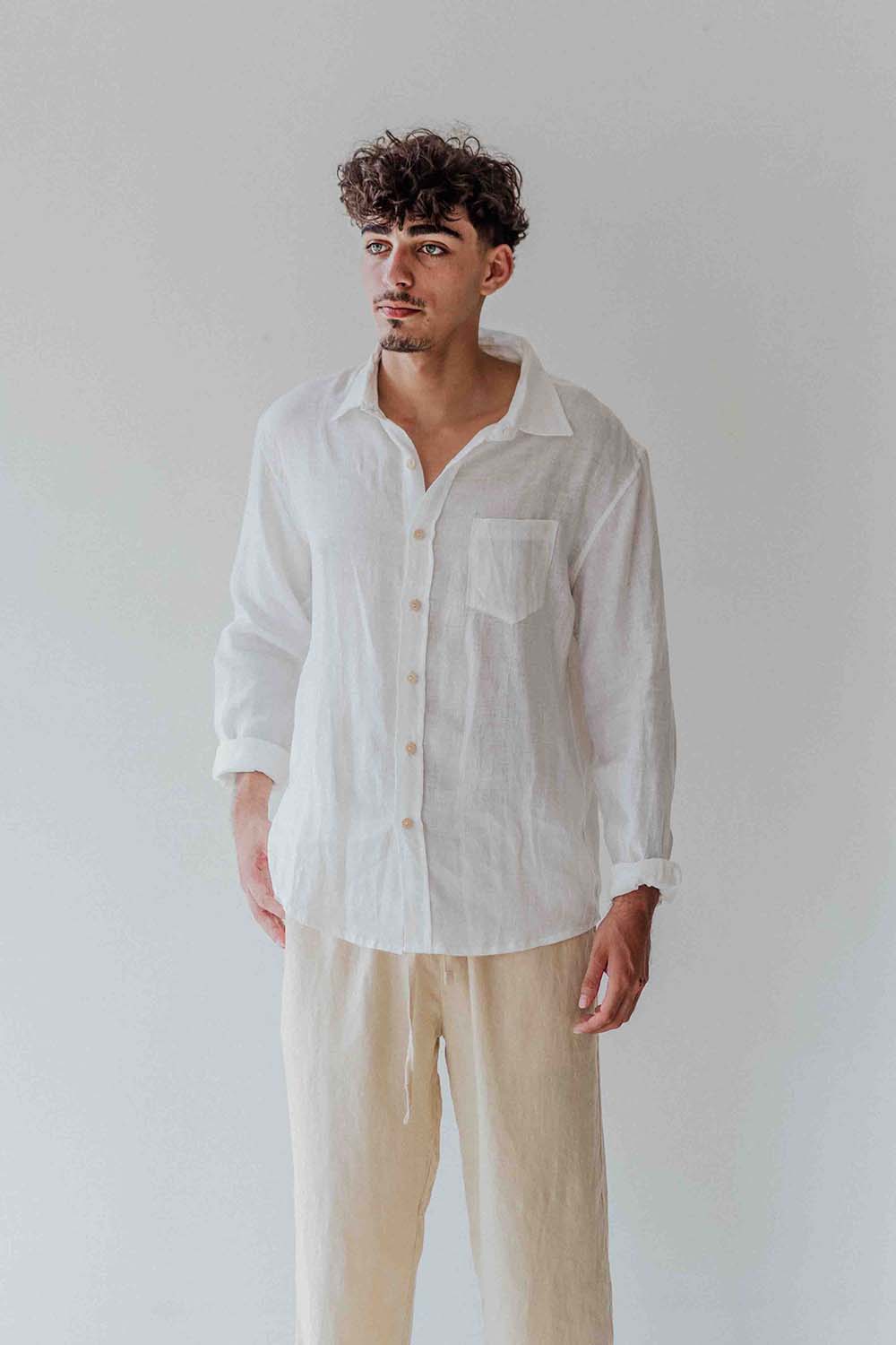 Man wearing a white linen shirt and beige pants against a plain background