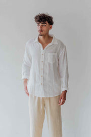 Man wearing a white linen shirt and beige pants against a plain background