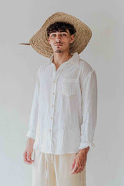 Man wearing a white shirt and straw hat against a plain background