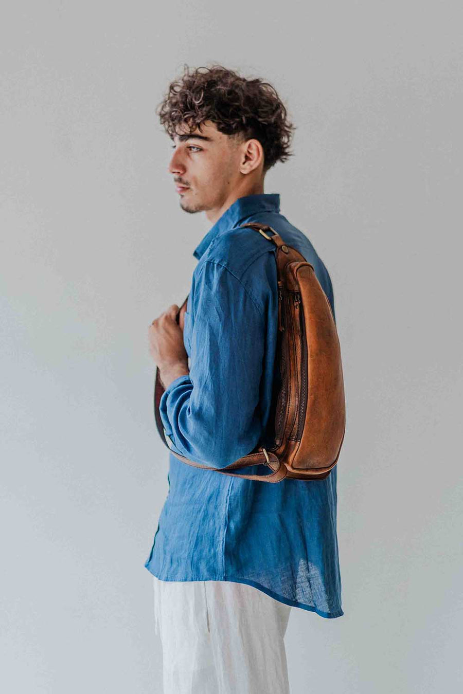 Man wearing a blue shirt with a brown leather backpack against a plain background