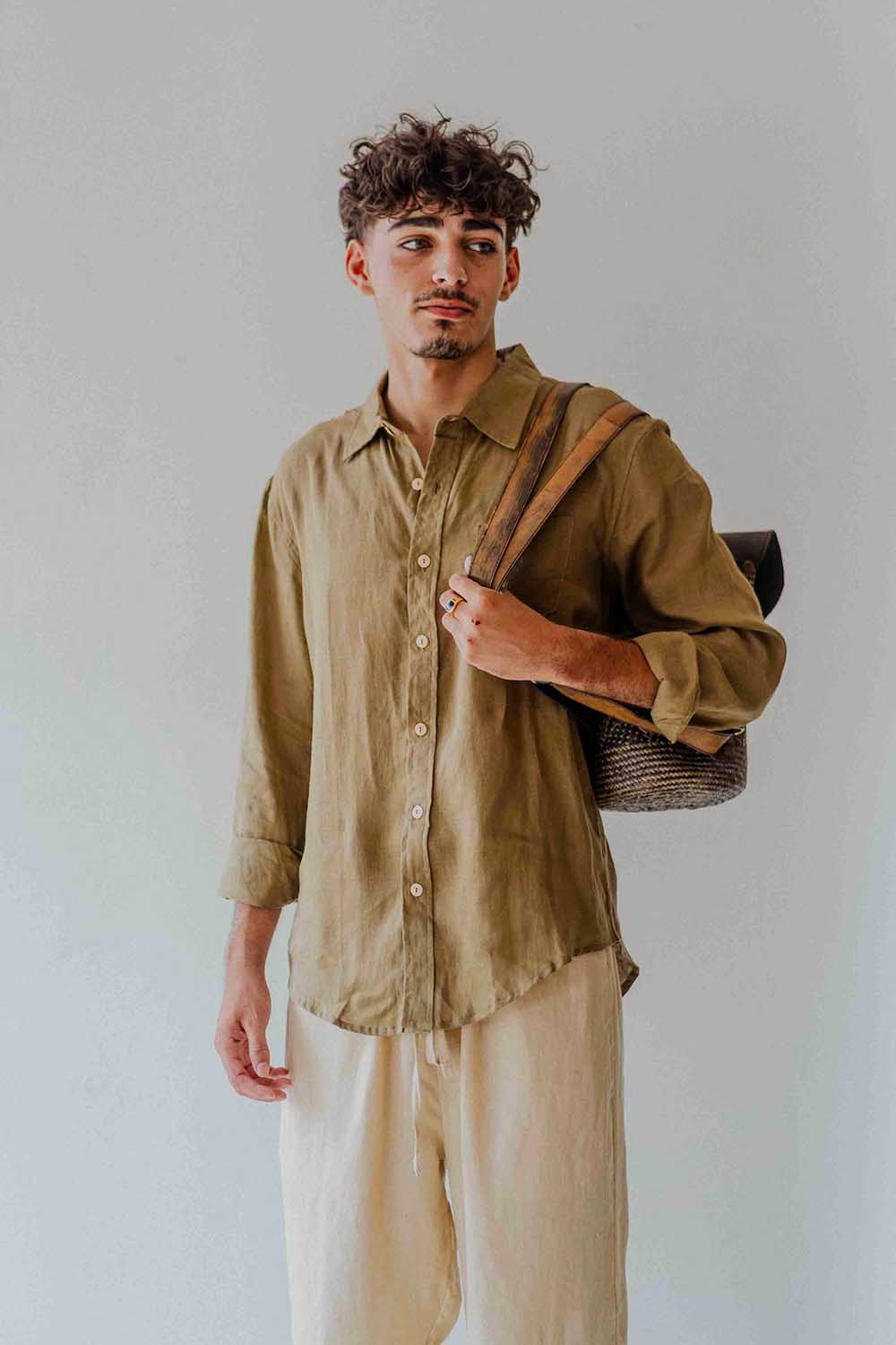Man wearing a green shirt and beige pants holding a bag against a plain background