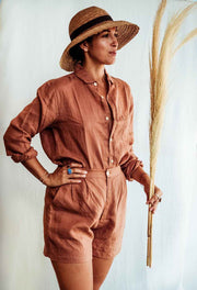 Person wearing a brown jumpsuit and hat, holding a broom against a light background