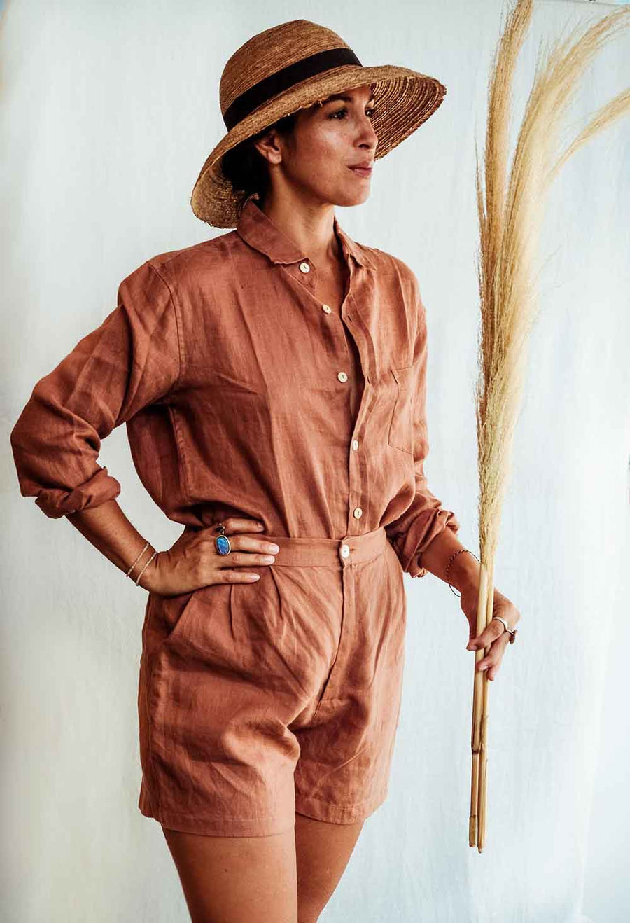 Person wearing a brown jumpsuit and hat, holding a broom against a light background