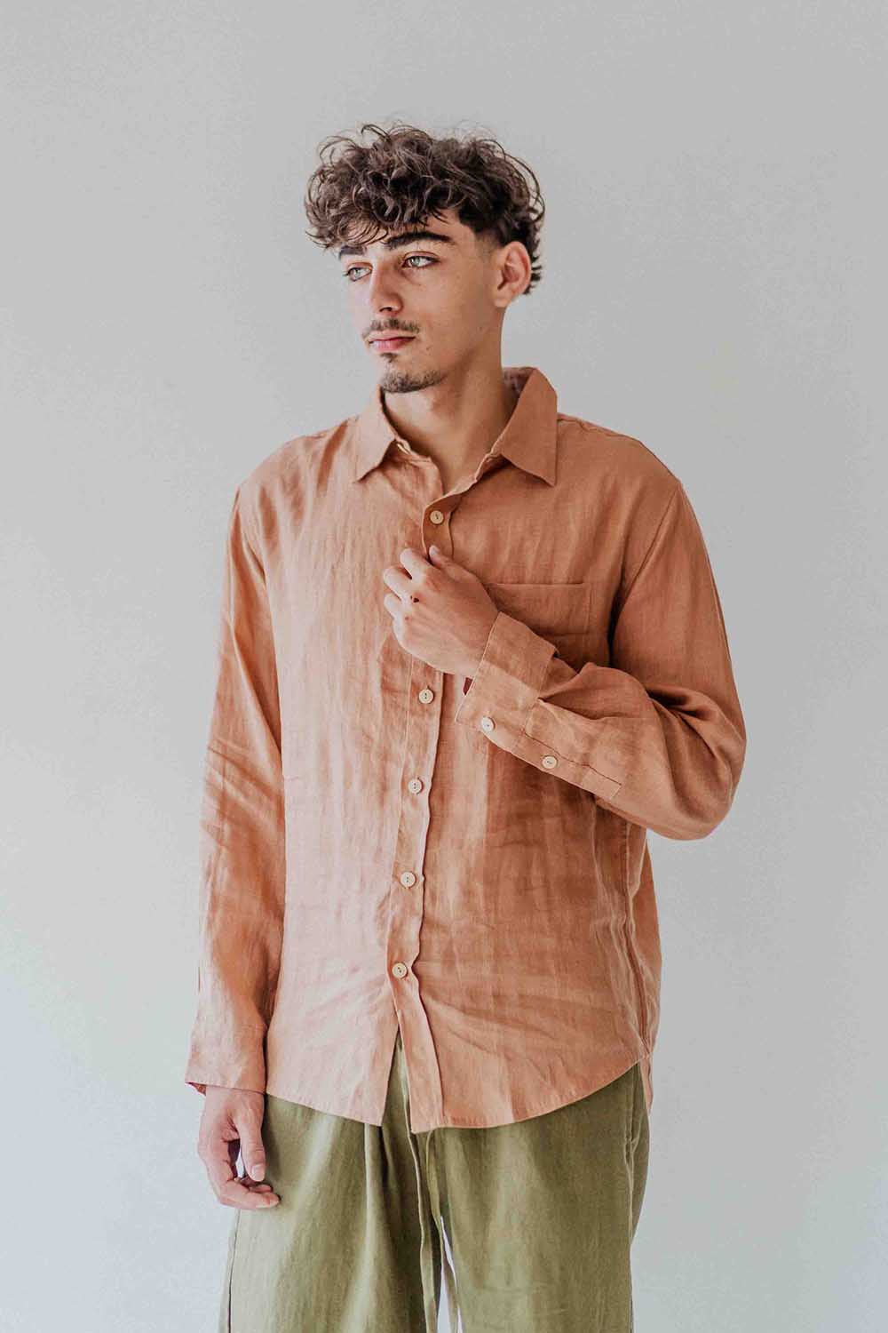 Man wearing a brown button-up shirt and green pants against a plain background