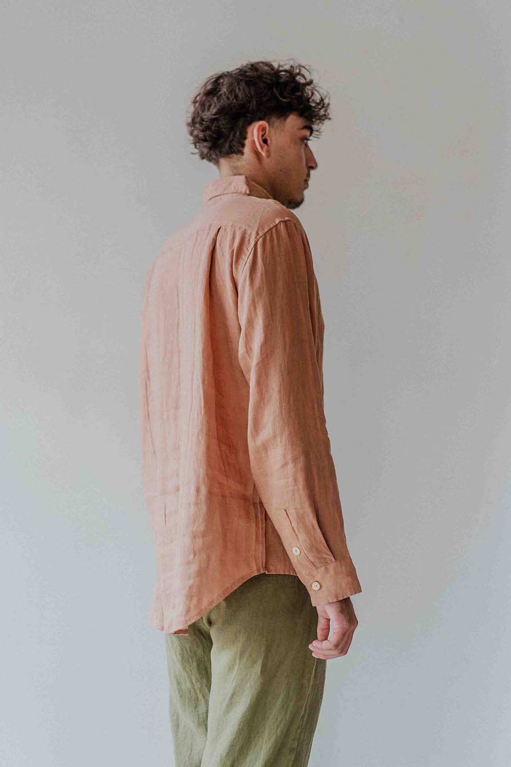 Man wearing a peach-colored shirt and green pants against a plain background
