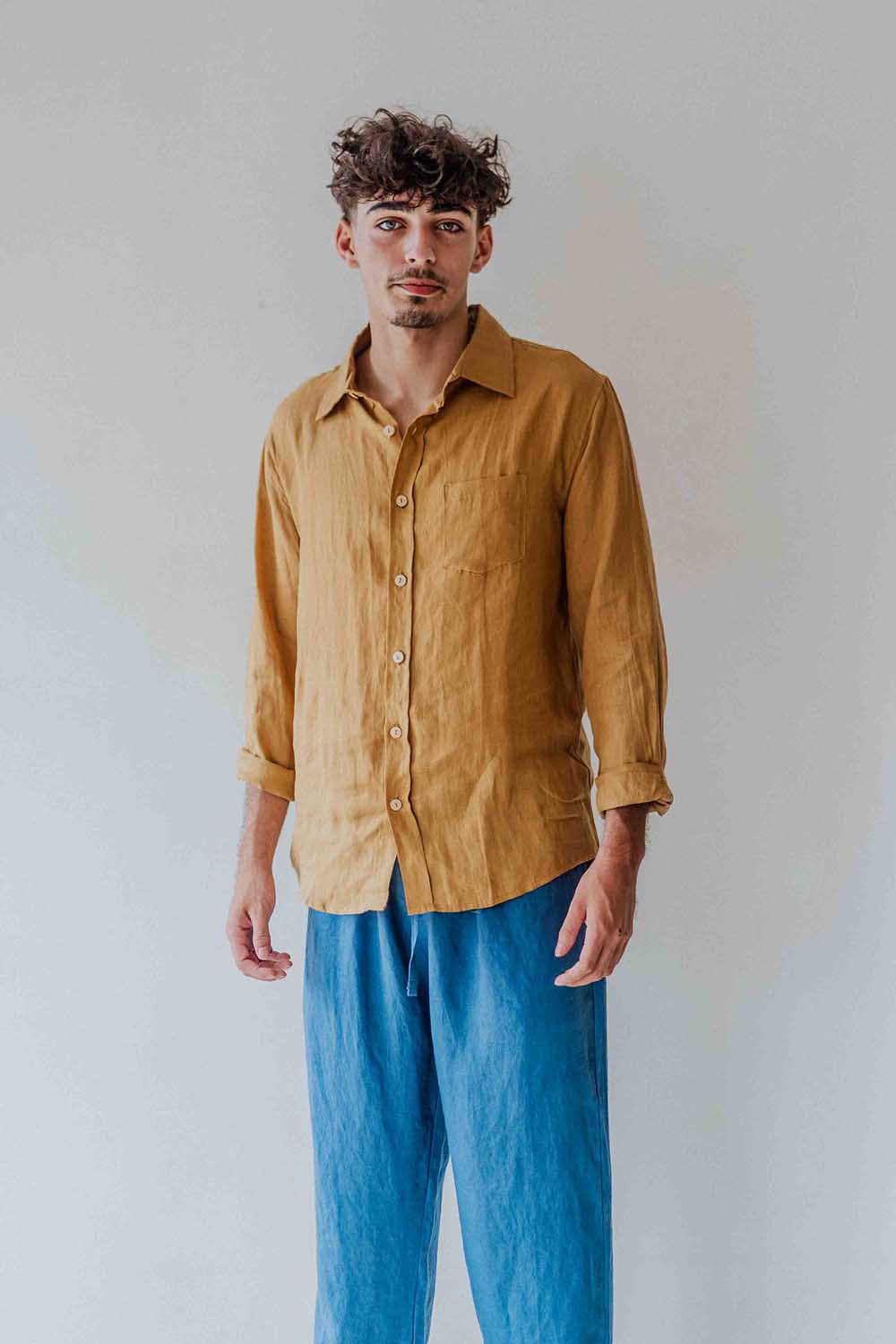 Man wearing a mustard yellow shirt and blue pants against a plain background