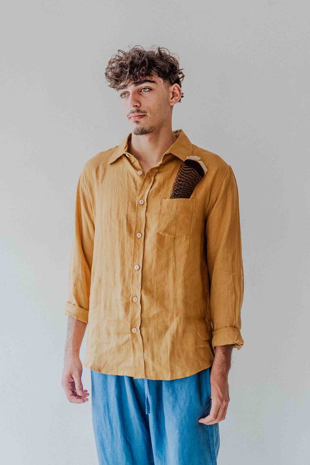 Man wearing a mustard yellow shirt with a pocket detail against a plain background