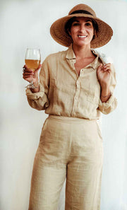Woman in beige linen outfit holding a glass of wine against a white background