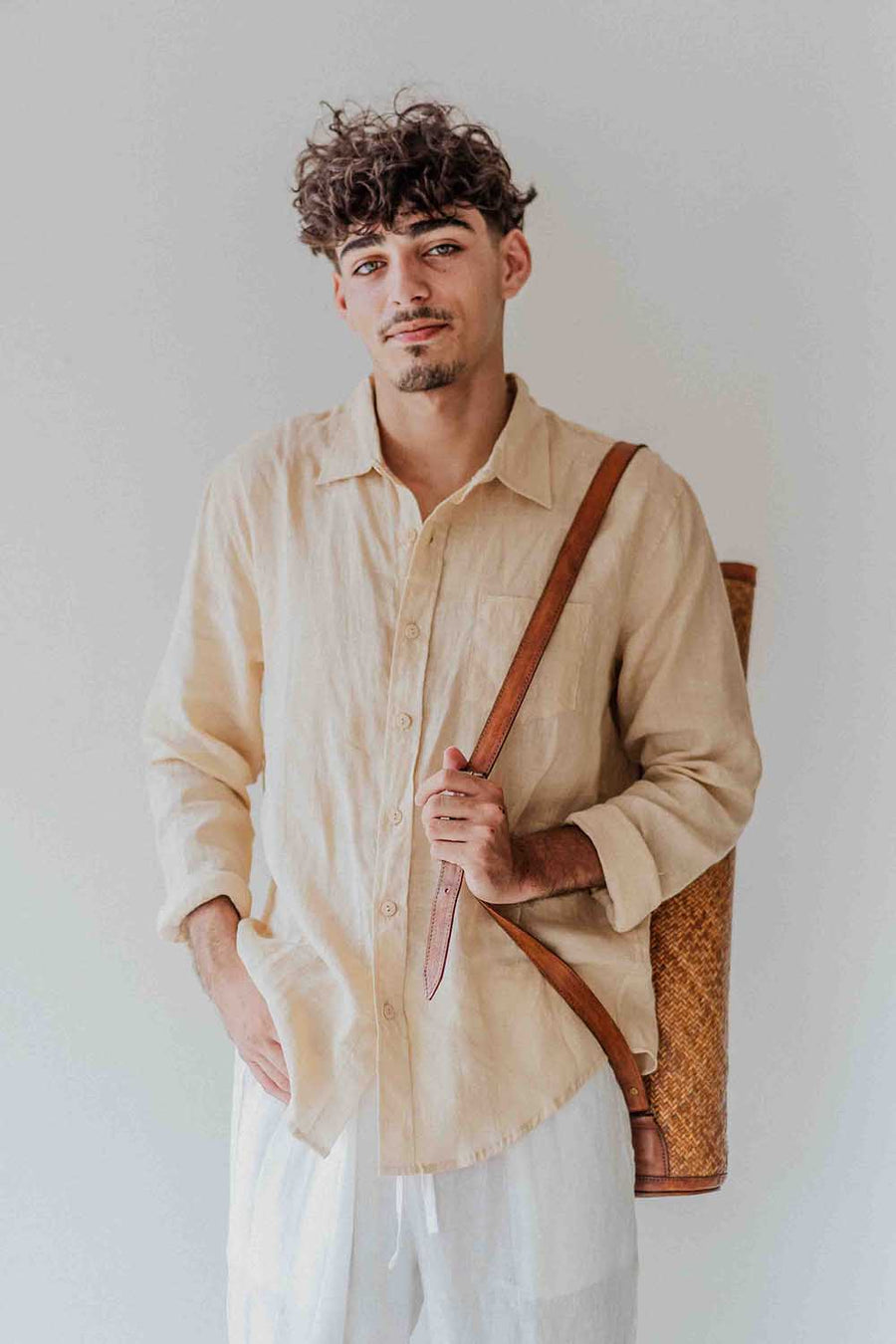 Man holding a brown leather bag against a plain background