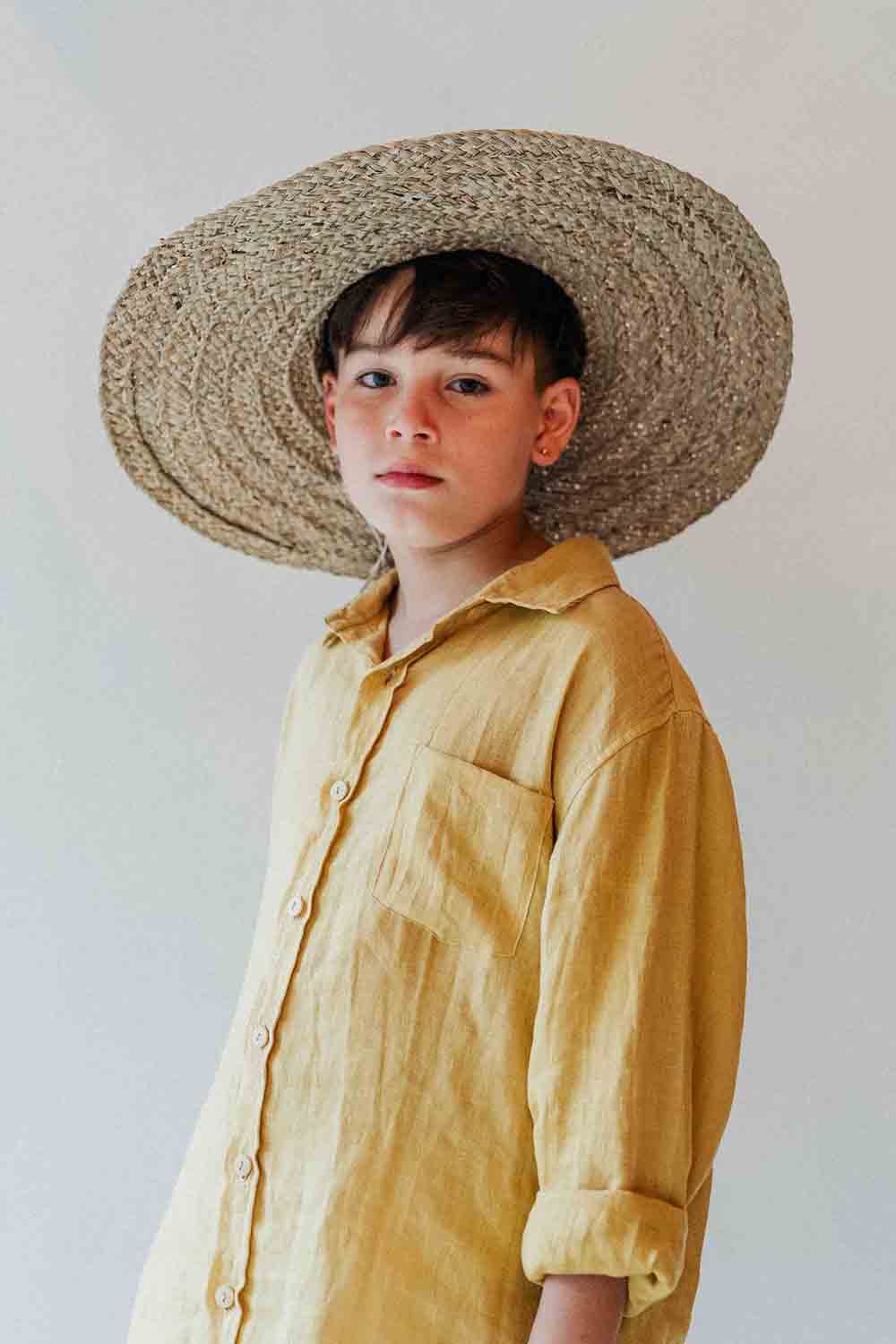 Child wearing a wide-brimmed straw hat and yellow shirt against a plain background