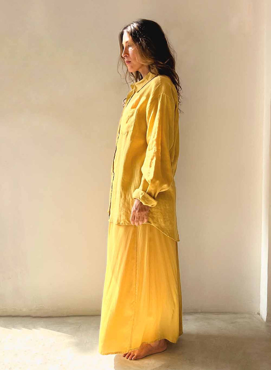 Woman wearing a yellow outfit standing against a plain wall.