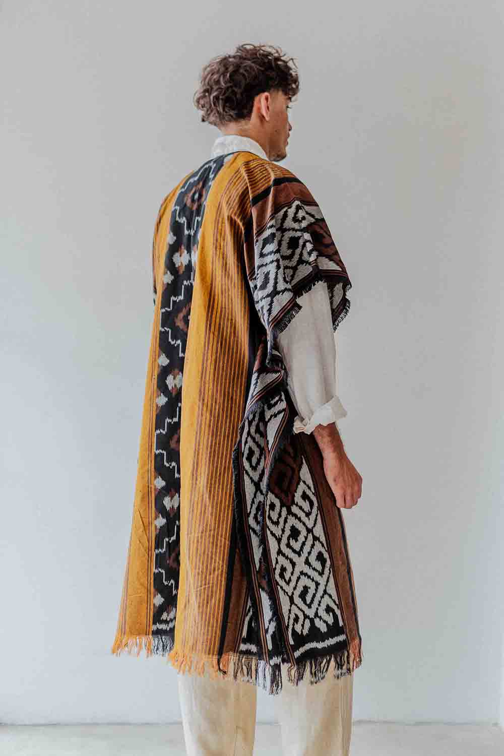 Person wearing a patterned shawl over a white shirt with a plain background